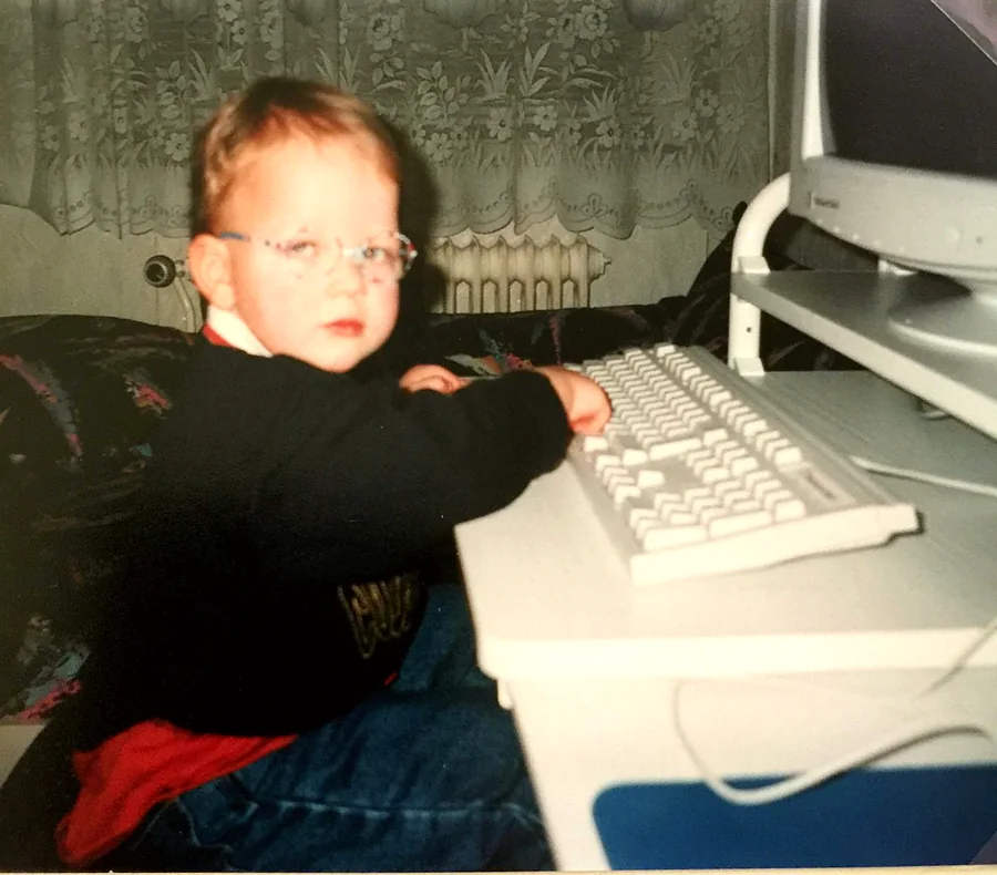 Arnold as a toddler wearing glasses, sitting at a computer keyboard