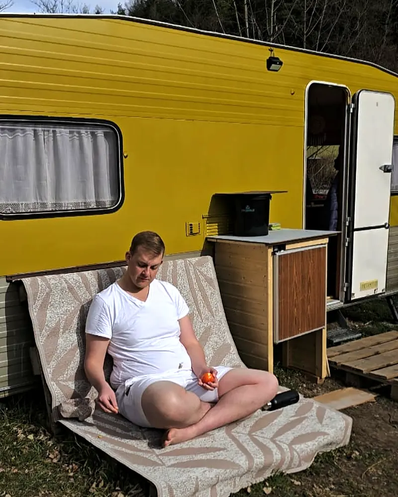 Arnold sitting on a lounger in front of a yellow caravan
